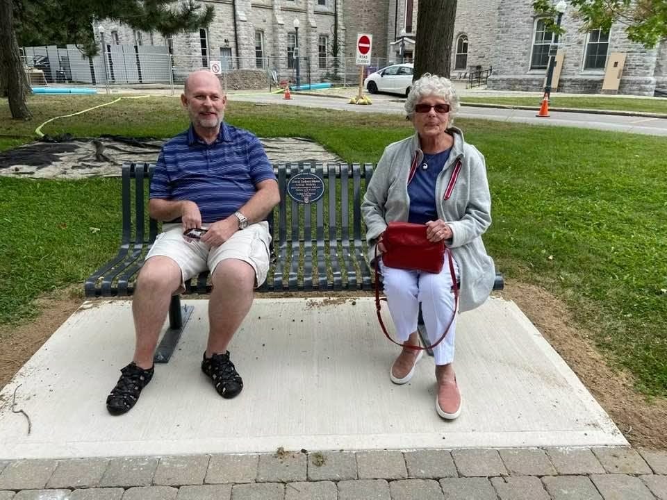 John-David Skene relaxing on a park bench outdoors beside a companion.